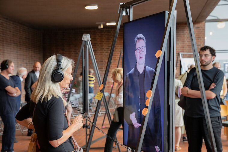 Eine Besucherin lauscht dem Interview mit Jens Hendrix, Baudezernent in Hattingen zu Kirchentransformationen. Ausstellungseröffnung „Kirchen als Vierte Orte – Perspektiven des Wandels“, 1.9.2024, Heilig-Geist-Kirche, Essen. Foto: Claudia Dreyße